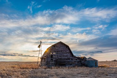 Saskatchewan, Kanada 'da eski ahır, çöp bidonu ve yel değirmeni üzerinde gün batımı 