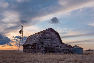 Saskatchewan, Kanada 'da eski ahır, çöp bidonu ve yel değirmeni üzerinde gün batımı 