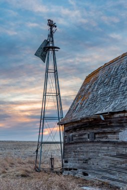 Saskatchewan 'da eski bir ahırın yanındaki kırık bir yel değirmeninin üzerinde gün batımı.