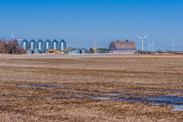 Field and farmyard with grain bins and a large vintage barn surrounded by wind turbines in Saskatchewan, Canada
