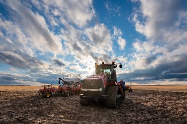 Swift Current, SK / Kanada - 9 Mayıs 2020: Vaka traktörünü ve Bourgault hava dölleme ekipmanlarını kontrol eden bir çiftçinin günbatımı gökyüzü 