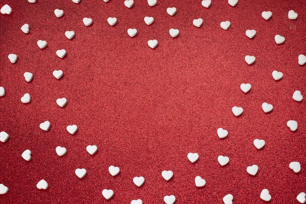 Rama białych cukierków w kształcie serca na czerwonym, błyszczącym tle — Zdjęcie stockowe