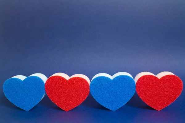 Four red and blue heart shape dishwasher sponge in the foreground on the blue background — Stok fotoğraf