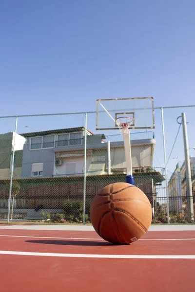 Используемый баскетбол на переднем плане лежит на баскетбольной площадке и баскетбольной корзине с размытым фоном Лицензионные Стоковые Фото
