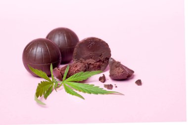Çikolata şekerler ve pembe arka planda bir yaprak marihuana. Haşhaş yağı eklenmiş tatlı şekerler.