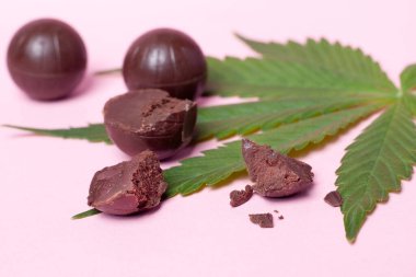 Çikolatalı şekerler, çikolatalı şekerler ve pembe bir arka planda marihuana yaprağı.