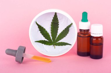 Marihuana özü ilaçları. Pembe arka planda thc ve cbd içeren yeşil yaprak ve kenevir yağı