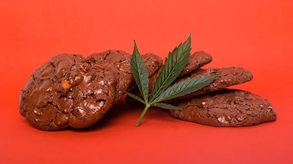 Sladkosti s marihuanou na červeném pozadí. konopné sušenky a zelený list — Stock fotografie