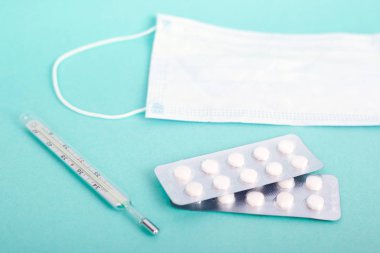 high temperature , high fever for colds. antiviral medical products. pills, thermometer, mask on a blue background