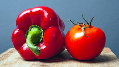 Domates ve kırmızı kırmızı biber, gri arka planda ahşap bir tabakta. taze sağlıklı sebzeler