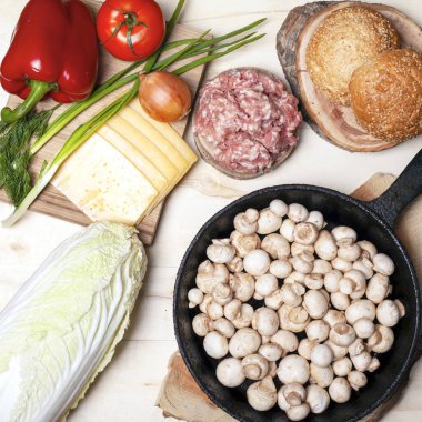 Hamburger, çörek, mantar, sebze ve et için taze çiğ yiyecekler.