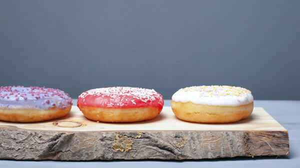 multicolored assorted red,white,violet donuts coated with glaze and sprinkled with Easter powder on a wooden stand on a gray background, sweet eco food 