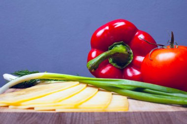 Otlu sebzeler ve peynirle ahşap bir tezgahın üzerinde gri bir arka plan. Çan biberi domates ve yeşil soğan. Yakın çekim