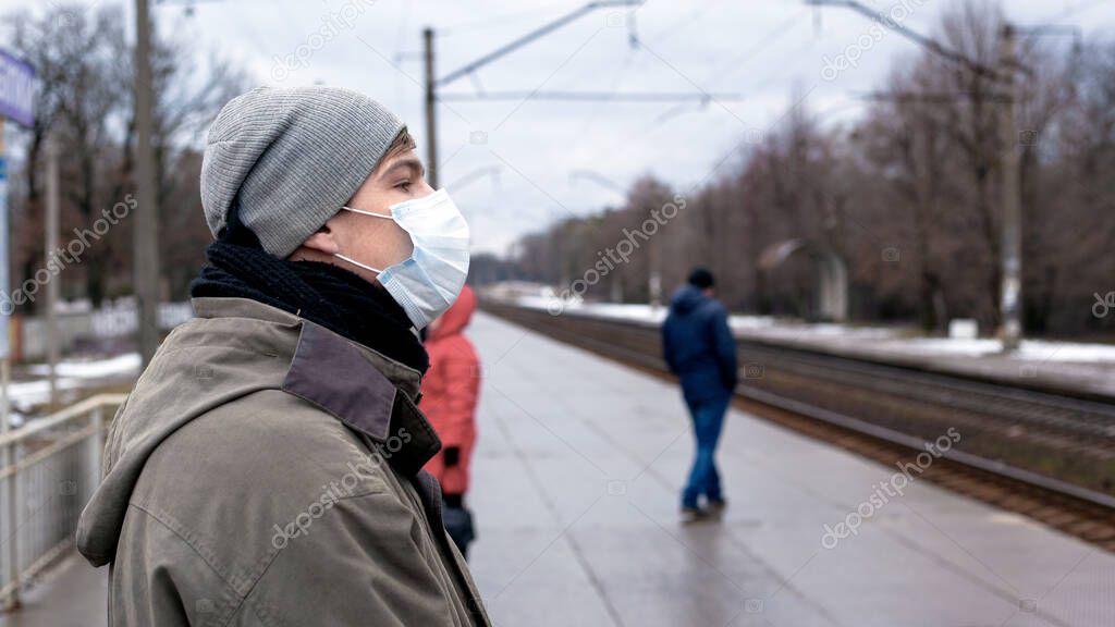 young guy in a medical disposable bandage on a crowded platform of the station. protection against respiratory viral diseases