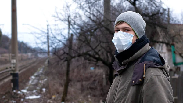 Junger Mann mit medizinischer Einmalmaske, der in der Nähe des Bahnhofs steht. Virusgrippe, SARS, Covid-19 — Stockfoto