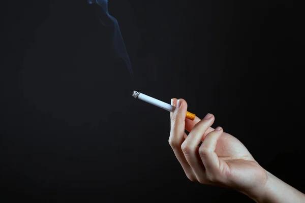 Mão feminina segurando um cigarro fumando em um espaço de cópia de fundo escuro. danos causados pelo fumo de cigarros — Fotografia de Stock