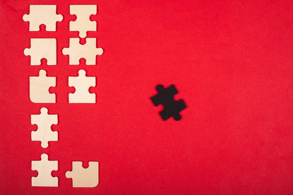 Puzzle di legno di colore bianco e nero su uno sfondo rosso vista dall'alto. spiccano, leader — Foto Stock
