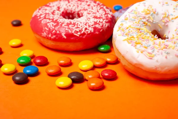 Glaserade röda och vita runda bullmunkar och flerfärgade sötsaker på orange bakgrund. snacks för barn — Stockfoto