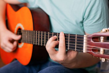 Adam akustik gitar çalıyor, parmakları bar akoru tutuyor. Bir müzik aleti çalmayı öğren.