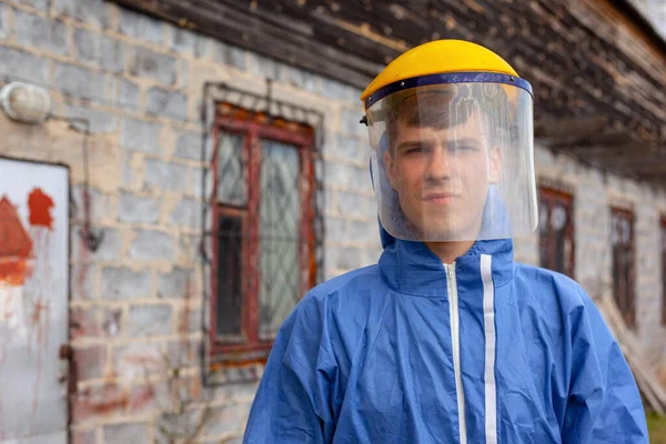 Junger Mann in blauem Schutzanzug und mit medizinischer Plastikmaske steht in der Nähe des Gebäudes — Stockfoto