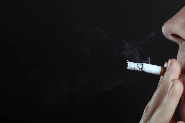 Hombre fuma un cigarrillo en un fondo oscuro espacio de copia de cerca, peligro para la salud, daño al cuerpo por el consumo de tabaco, mal hábito —  Fotos de Stock