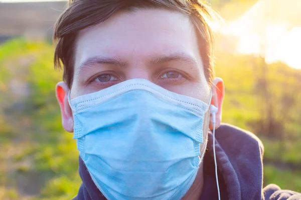 Porträt eines jungen Mannes in medizinischer Maske in den Frühlingsstrahlen der Sonne aus nächster Nähe. Quarantäne, Coronavirus-Pandemie covid-19 — Stockfoto