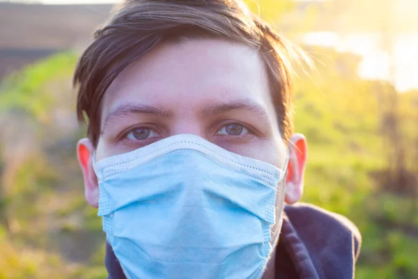 Mann in medizinischer chirurgischer Schutzmaske im Freien in der Sonne in Großaufnahme. Quarantäne-Pandemie, Ausbruch der Coronavirus-Grippe covid-19 — Stockfoto