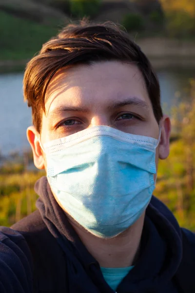 Mann in medizinischer OP-Maske im Freien in der Sonne in Großaufnahme. Schutzmaßnahme während der Quarantäne, Coronavirus-Pandemie Covid-19 — Stockfoto