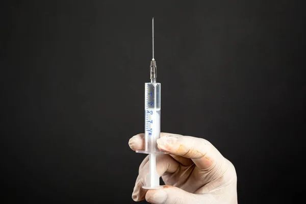 Hand in een wegwerp steriele witte handschoen met een medische spuit van 5 ml op een donkere achtergrond close-up. een injectie behandeling schoot — Stockfoto