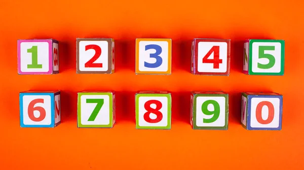 Wooden cubes with numbers exactly stacked on an orange background top view close-up developing a toy Royalty Free Stock Images