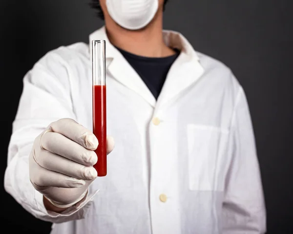 doctor in a white coat with disposable gloves and a medical mask holding a test tube in his hand with infectious blood.