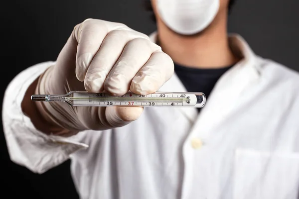 Arts in een witte vacht en masker houdt een thermometer ziekte check virus covid-19 griep koude close-up — Stockfoto