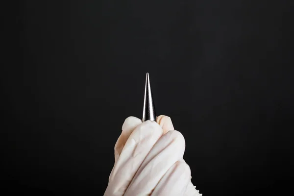 Hand in a white disposable glove ear expander for piercing tunnels on a dark background close-up — Stock Photo, Image