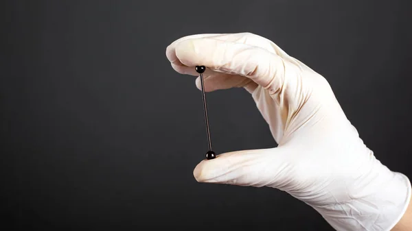 Beyaz steril bir eldivenin içinde koyu bir arka planda kıkırdak kulak takısı için piercing bulunur. — Stok fotoğraf