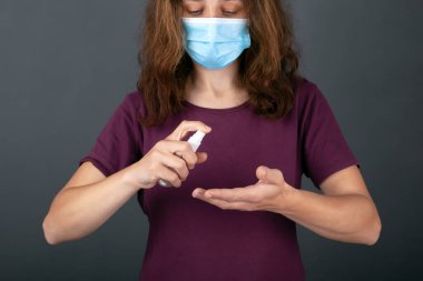 Tıbbi maskeli bir kız ellerini antiseptik spreyle dezenfekte ediyor. Covid-19 koruması. Hijyen, enfeksiyon önleme