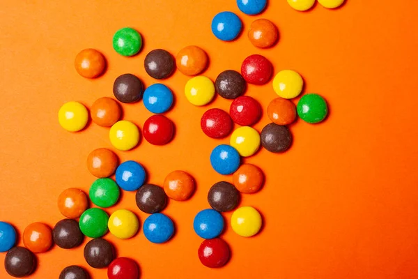 Comida de vacaciones chocolate multicolor pequeños dulces dispersos en un fondo naranja vista superior de cerca — Foto de Stock