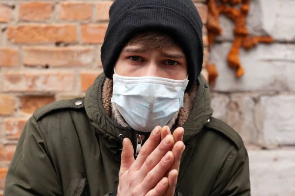 Mann mit medizinischer Maske steht auf dem Hintergrund einer Ziegelmauer und hält die Hände zusammen. Ausbruch des Coronavirus COVID-2019 — Stockfoto