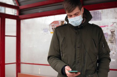 Tıbbi maskeli bir adam otobüs durağında duruyor. Viral hastalıklardan korunmak için izole edilmiş. Coperid-19. Kızamık gribi. Suçiçeği.
