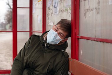 Adam tıbbi maskeyle otobüs durağında uyuyor. Yakın plan solunum viral hastalıklarını koruyor. Grip virüsünü önlüyor.