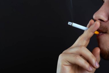 Elinde yanan bir sigara tutan adam arka planda duman soluyor. Nikotin fotokopi alanından gelen sigara zararları