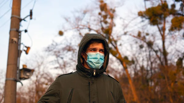 Ein junger Mann mit medizinischer Schutzmaske steht auf der Straße. Pandemie in Quarantäne-Isolation. Ausbruch der Coronavirus-Grippe — Stockfoto