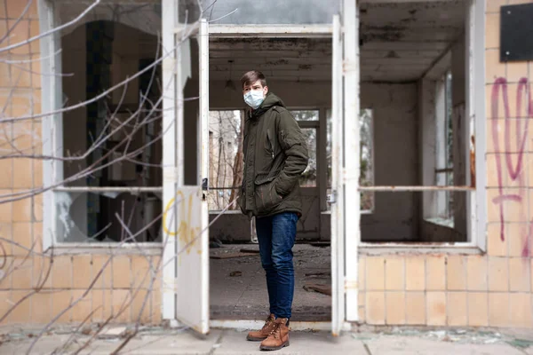 Ein junger Mann mit medizinischer Maske steht am Eingang eines verlassenen Krankenhausgebäudes. Seuchenschutz — Stockfoto