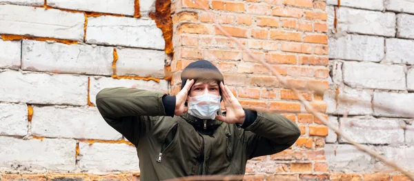 Pria bertopeng steril medis berdiri di dinding bata memegang tangan di atas kepala. pandemi coronavirus — Stok Foto