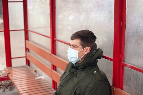 Öffentlicher Coronavirus-Schutz. Virusausbruch bis 2019. Ein Mann mit einer medizinischen Schutzmaske wartet auf einen Bus — Stockfoto