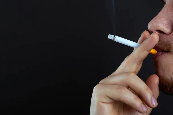Chlap držící hořící cigaretu vdechuje kouř na tmavém pozadí. kouření poškození z nikotinu kopírovat prostor close-up — Stock fotografie