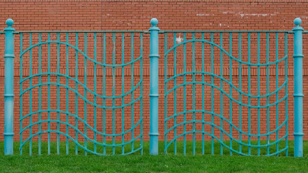 Aqua modrý vlnitý plot postavený na travnaté ploše s červenou cihlovou zdí za — Stock fotografie