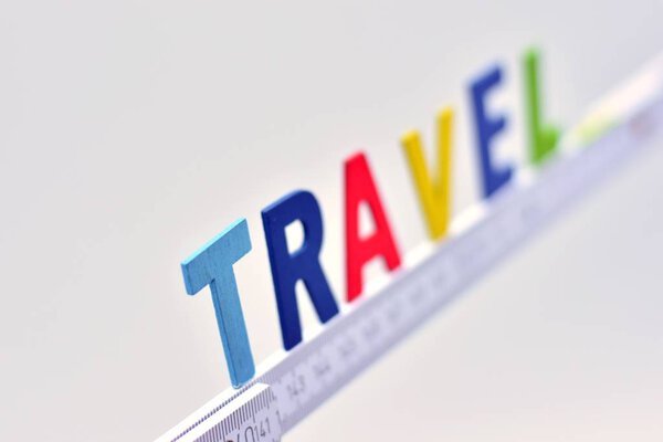 The word travel, made with wooden letters on a white carpenter's meter