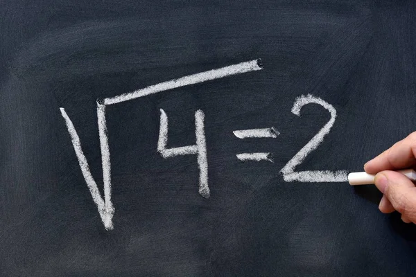 Hand writing the square root of four with a chalk on the blackboard