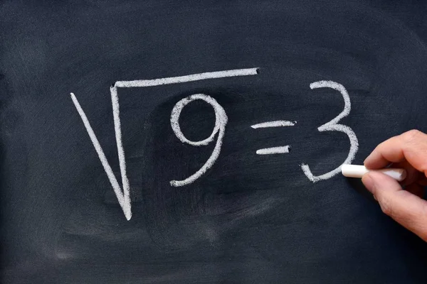 Hand writing the square root of nine with a chalk on the blackboard