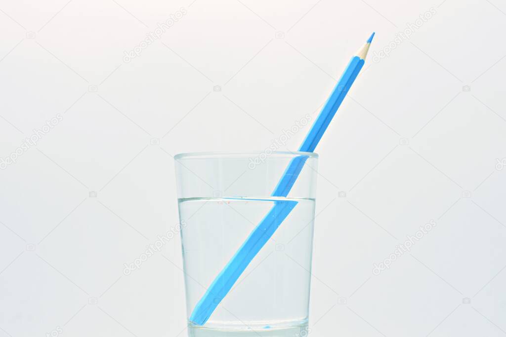 Blue colored pencil inside a glass of water, light refraction